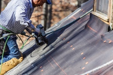 Worker installing shingles on a residential roof using a nail gun