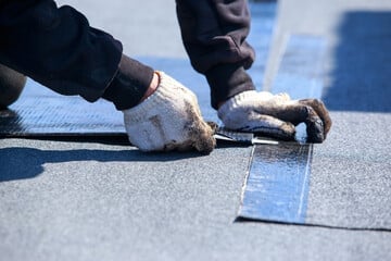 Workers hands applying roofing material along a blue chalk line on an asphalt surface